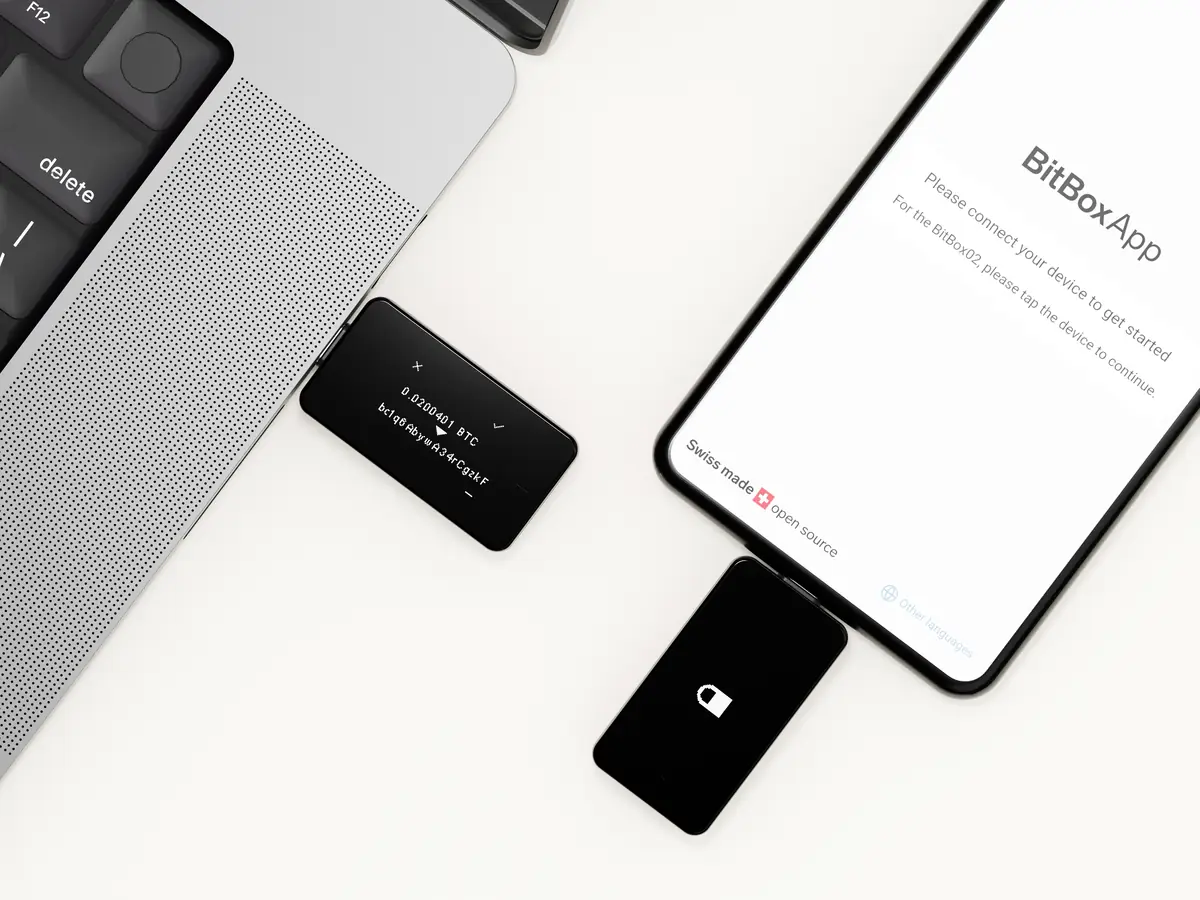 BitBox02 hardware wallet shown connected to laptop alongside BitBoxApp on a phone displaying Swiss made open source branding